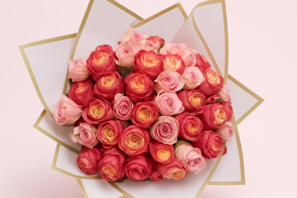 Runder, handgehaltener Strauß aus vielen hellrosa und pinken, dicht gefüllten Rosen in heller Papiermanschette mit Goldrand