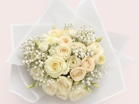 Rund gebundener Strauß mit cremefarbenen Rosen, Ranunkeln, weißen Lisianthusblüten und feinem Schleierkraut in weißer Verpackung